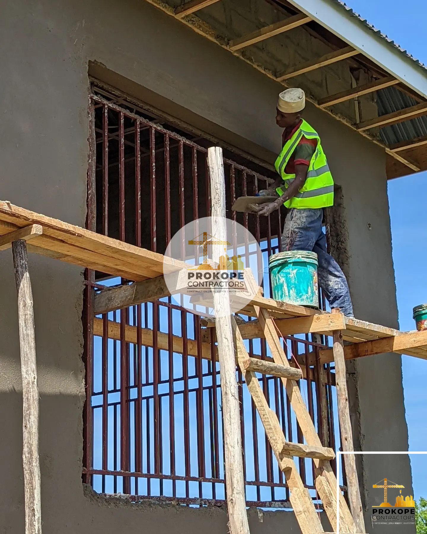 Worker in a high-visibility vest plastering a wall from timber scaffolding beside barred window openings