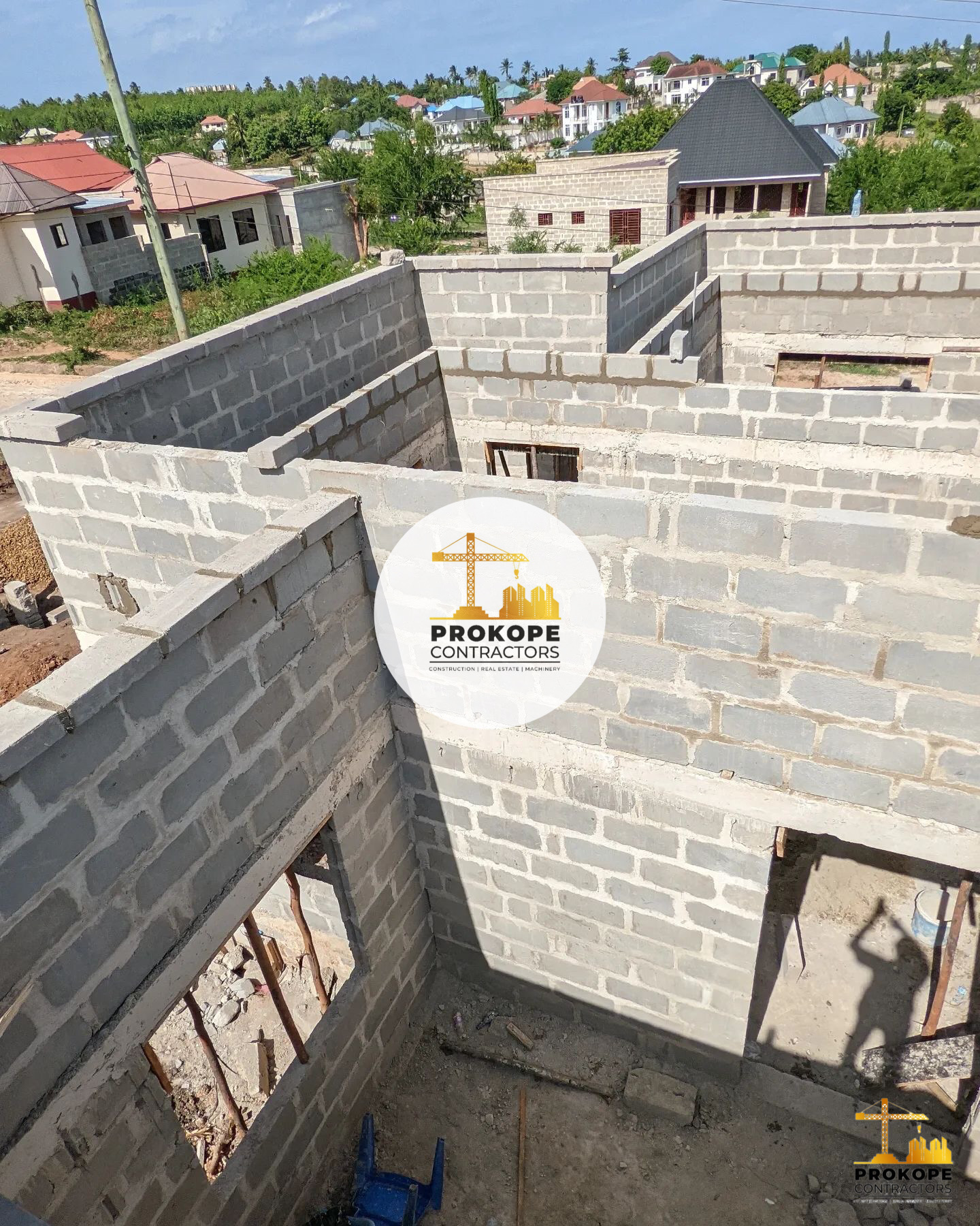 Blockwork walls of a house under construction seen from above, with door openings formed and a neighbourhood beyond