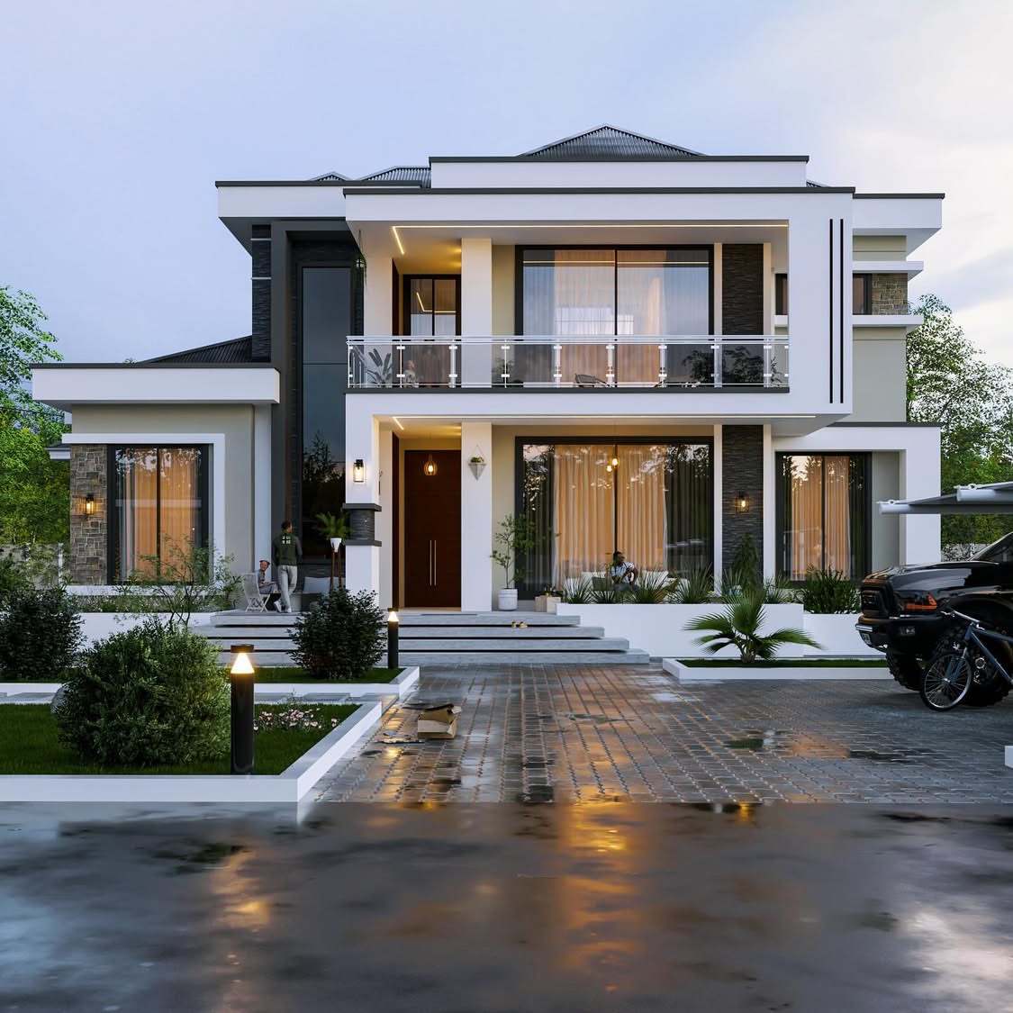 Symmetrical white and stone residence at dusk with a lit entrance, balcony above and a wet paved driveway reflecting the lights